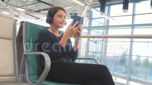 机场候机大厅供飞机飞行戴着耳机听音乐的年轻快乐少女视频的预览图
