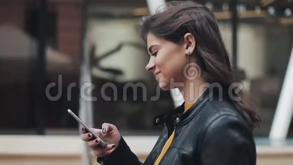 年轻快乐的女人在城市街道上散步同时使用智能手机慢动作视频的预览图
