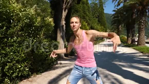 一个年轻快乐的家伙跳现代芭蕾在一个夏天的公园里打盹慢分子视频的预览图