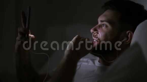 有智能手机和耳机的男人在床上过夜视频的预览图