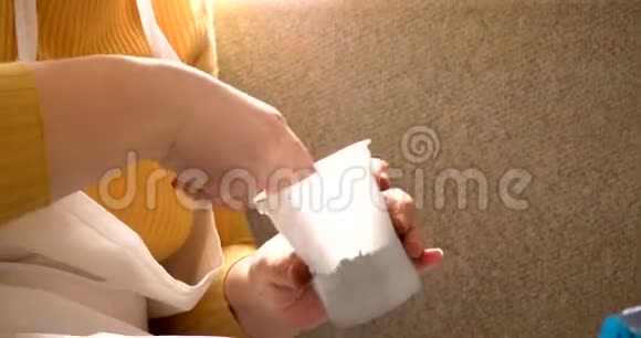 穿着白色围裙的女孩坐在家里窗户附近的白色塑料盆里女人用红色的水浇他们视频的预览图