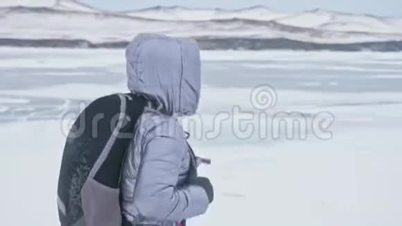 贝加尔湖冰上女子旅行去冬岛旅行女孩走在冰岩脚下旅行者看着视频的预览图