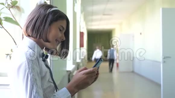 在学校概念上使用智能手机的女学生教育十几岁的小女孩用智能手机站在窗口视频的预览图