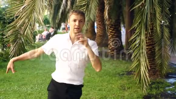一个年轻快乐的家伙跳现代芭蕾在一个夏天的公园里打盹慢分子视频的预览图