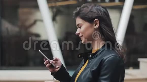 年轻快乐的女人在城市街道上散步同时使用智能手机慢动作视频的预览图