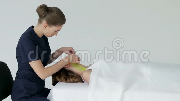 医生美容师在躺着的病人脸上贴胶带视频的预览图