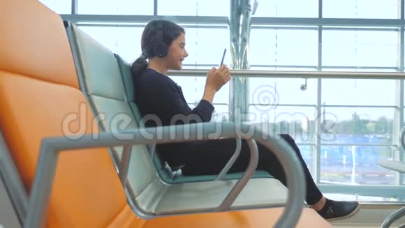 机场候机大厅供飞机飞行年轻快乐的生活方式戴着耳机听音乐的少女视频的预览图
