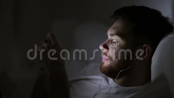 有智能手机和耳机的男人在床上过夜视频的预览图