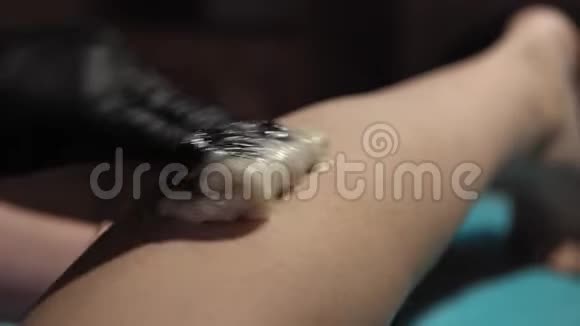 美容师从一个年轻女人的腿上取下头发糖膏视频的预览图