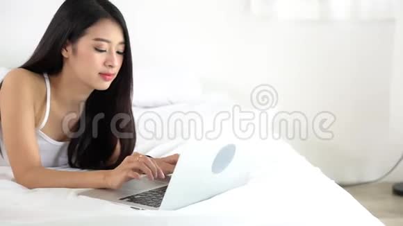 美丽的亚洲年轻女子躺在床上用笔记本电脑在卧室休闲放松视频的预览图