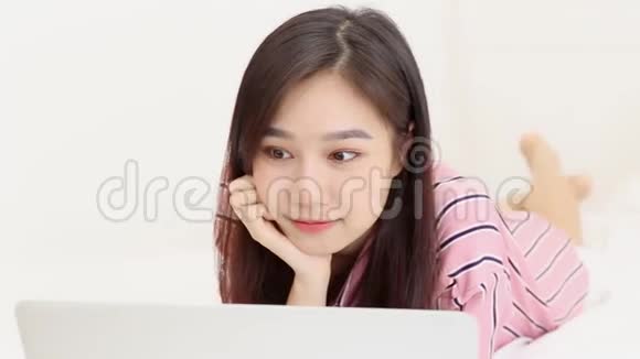 美丽的亚洲年轻女子躺在床上用笔记本电脑在卧室休闲放松视频的预览图
