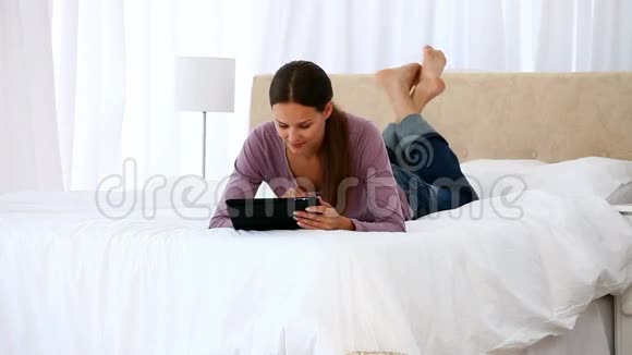 美丽的女人躺在床上用电脑平板电脑视频的预览图