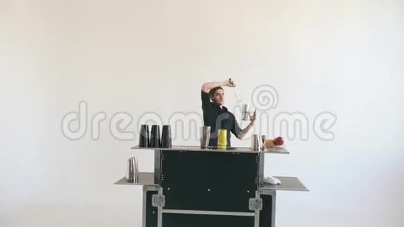 职业酒保男子在白色背景的移动酒吧桌上摆弄瓶子和摇晃鸡尾酒视频的预览图