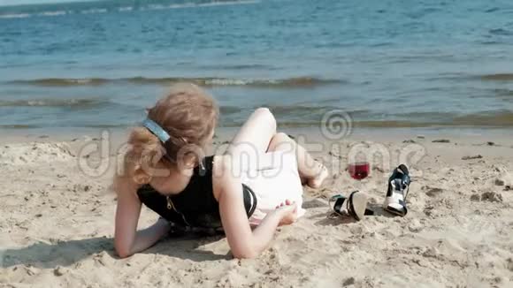 年轻的金发女郎穿着一件漂亮的裙子在海边享受一杯粉红色的葡萄酒动作非常缓慢视频的预览图