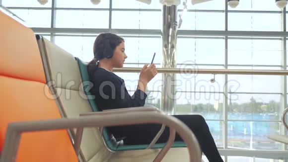 机场候机大厅供飞机飞行年轻快乐的少女戴着耳机听音乐视频的预览图