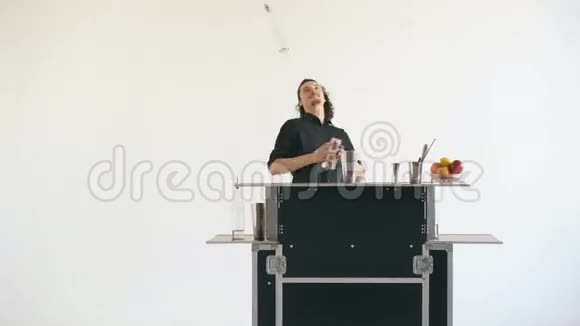 教授调酒师男子在白色背景的移动酒吧桌上摆弄瓶子和摇鸡尾酒视频的预览图