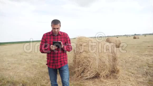 智慧农业理念男人的生活方式农民在数字平板电脑上的田野里研究干草堆慢动作视频的预览图