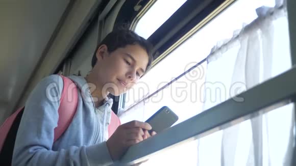 生活方式的少女旅行者带着背包站在火车的窗户边带着智能手机旅费视频的预览图