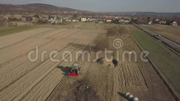一个农民在一辆红色拖拉机上带着播种机在村庄地区的一个私人田地里播种谷物春季机械化视频的预览图