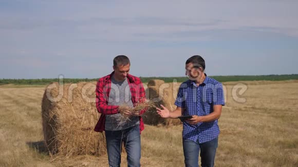 团队农业智慧农业理念两名男工农民在数字平板电脑上走在田里的干草堆上视频的预览图