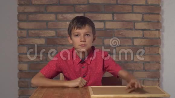 坐在桌子旁的孩子拿着挂图纸背景红砖墙上写着微笑视频的预览图