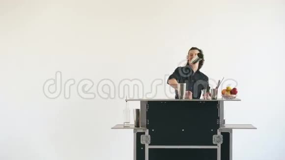 教授调酒师男子在白色背景的移动酒吧桌上摆弄瓶子和摇鸡尾酒视频的预览图