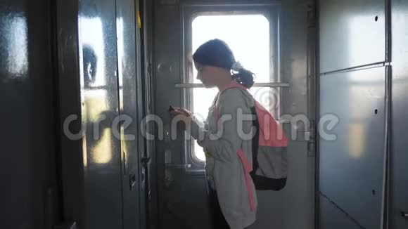 带背包的少女旅行者站在火车的窗户边手里拿着一部智能手机旅费视频的预览图