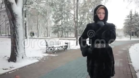穿着时髦貂皮大衣的年轻美女在冬季公园的背景下视频的预览图