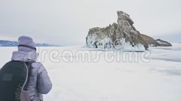 贝加尔湖冰上女子旅行去冬岛旅行女孩走在冰岩脚下旅行者看着视频的预览图