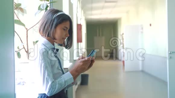 在学校概念上使用智能手机的女学生教育年轻的女孩用智能手机站在窗户旁边视频的预览图