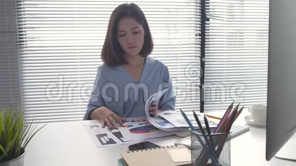 美丽的年轻微笑的亚洲女人在家里坐在客厅里用笔记本电脑工作视频的预览图