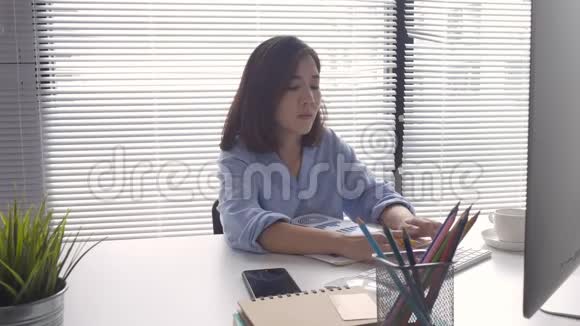 坐在家里客厅里用笔记本电脑工作的年轻漂亮微笑的亚洲女人视频的预览图