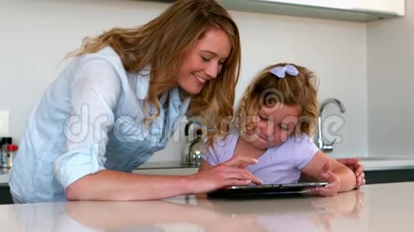 妈妈和女儿在厨房里用平板电脑视频的预览图