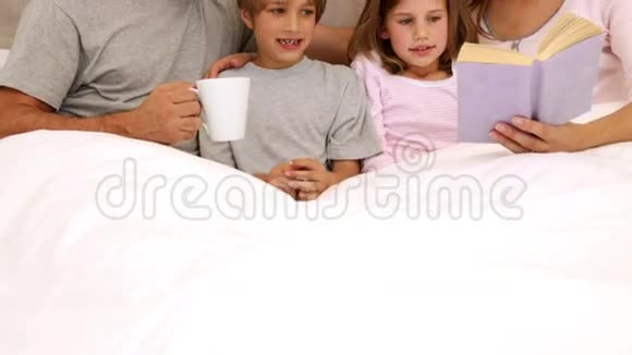 微笑的父母和孩子一起在床上看书视频的预览图