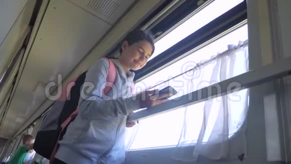 带着背包的少女旅行者站在装有智能手机的火车生活车的车窗旁旅行视频的预览图