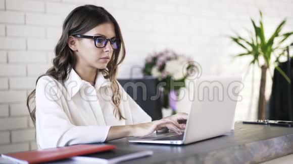 戴着眼镜在办公室里用笔记本电脑打字的年轻女子视频的预览图
