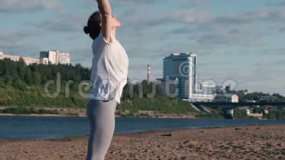 女人在城市河边的海滩上伸展瑜伽美丽的城市景色视频的预览图