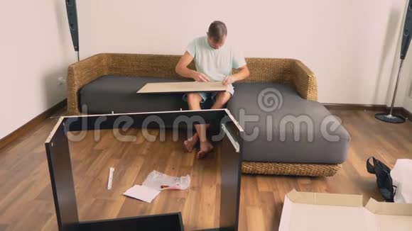 一个年轻人在他家的客厅里独立收集家具一个男人收集一张电脑桌视频的预览图
