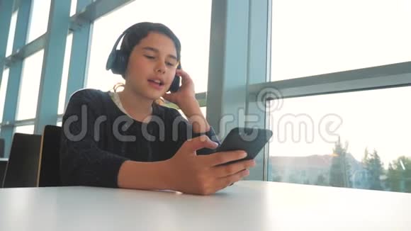 年轻快乐的十几岁女孩戴着耳机唱歌听着智能手机上的音乐社会中的少女生活方式视频的预览图