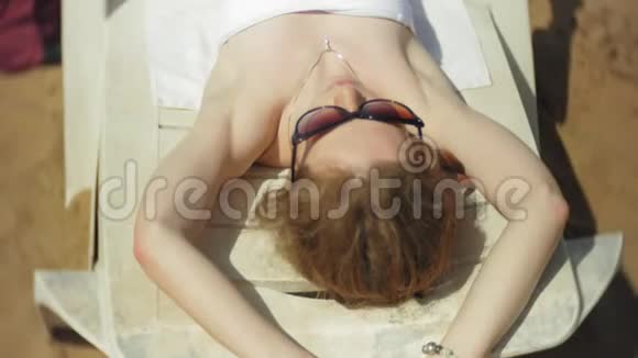 穿白色比基尼的年轻女孩躺在沙滩上的躺椅上晒太阳视频的预览图
