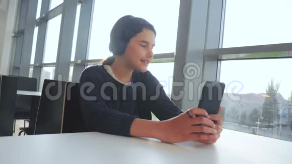 快乐的年轻少女戴着耳机唱歌听着智能手机上的音乐社交网络中的少女视频的预览图