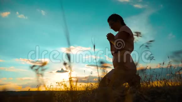 女孩在日落时双手交叉祈祷剪影慢动作录像女孩双手交叉祈祷祈求上帝视频的预览图