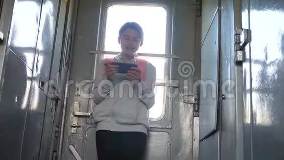 带背包的少女旅行者站在火车的窗户边手里拿着一部智能手机旅费视频的预览图
