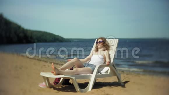 穿白色比基尼的年轻女孩躺在沙滩上的躺椅上晒太阳视频的预览图