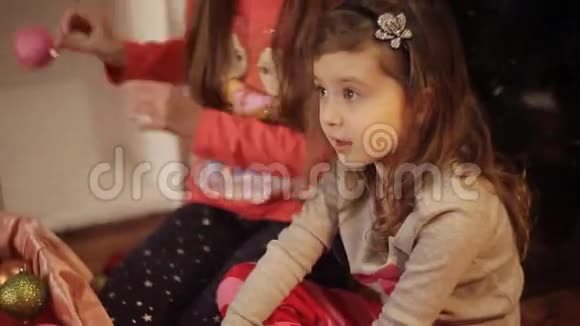 小女孩穿着舒适的家居服坐在地板上穿着漂亮的圣诞装饰品视频的预览图