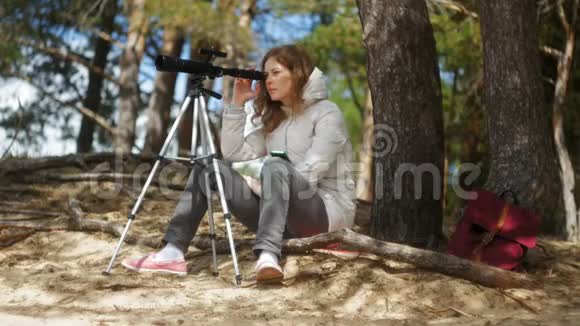 有魅力的女人在河岸的森林里通过望远镜看视频的预览图