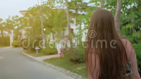 一个穿着蓝色连衣裙的年轻女孩正沿着热带城市的街道行走中弹慢动作视频的预览图