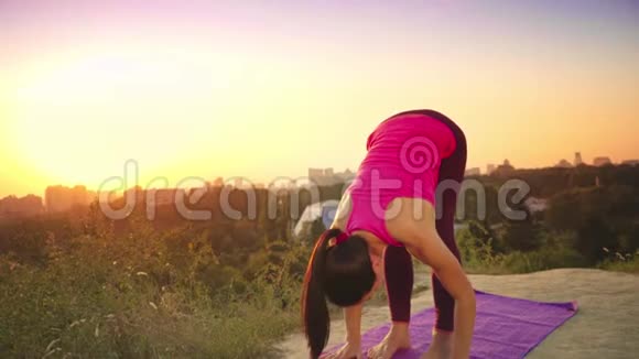 一个年轻的女人在大城市的背景下在山上练习瑜伽健康的女人在日落时做运动A视频的预览图
