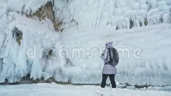 贝加尔湖冰上女子旅行去冬岛旅行女孩走在冰岩脚下旅行者看着视频的预览图