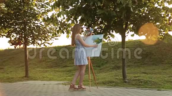 美丽的女孩在公园里画一幅画用颜料和铲子调色板带有图片的简易帆布视频的预览图